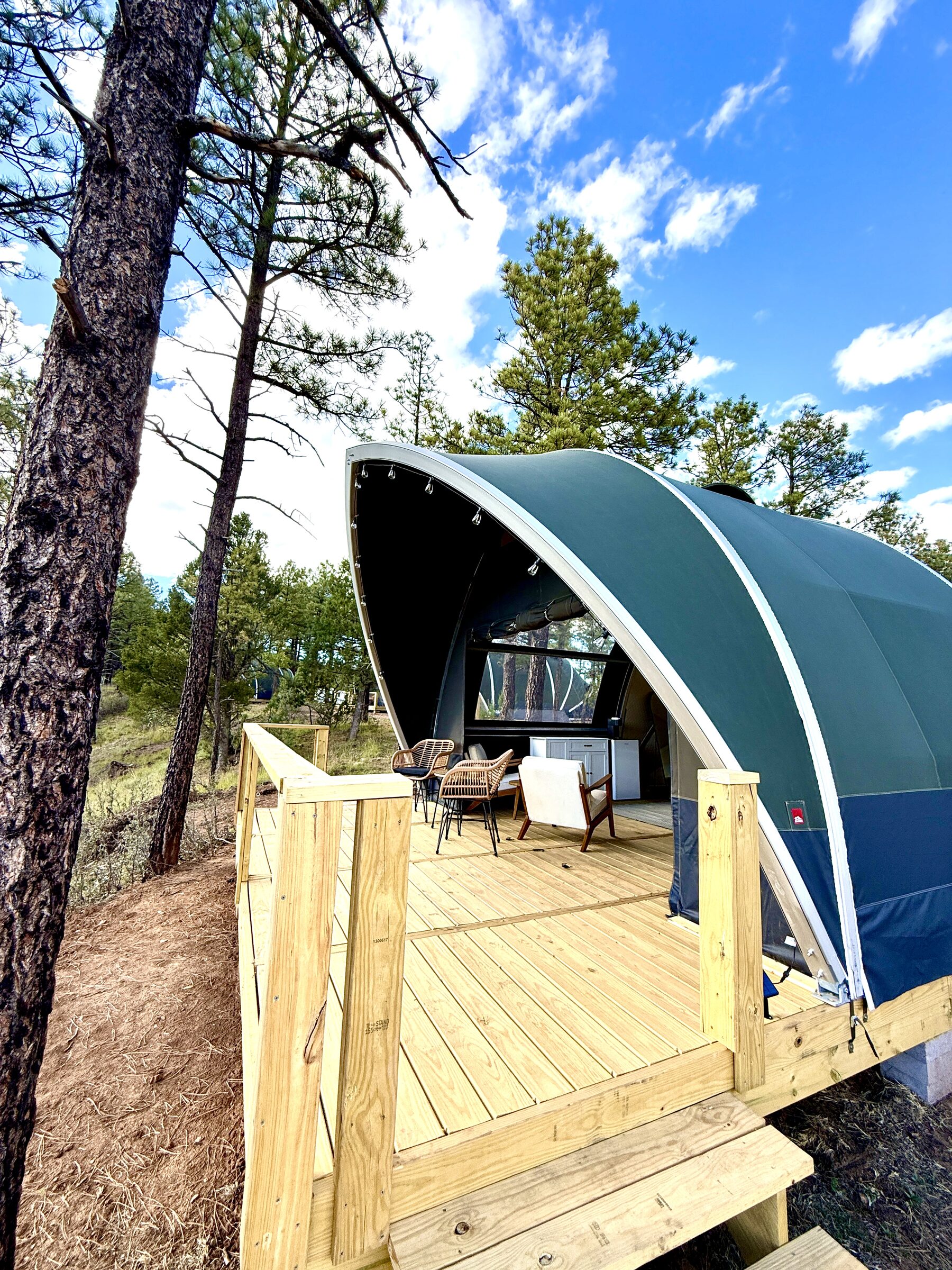 Glamping tent on an elevated wood platform built out over a sloped, wooded site